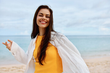 Wall Mural - Happy woman smile with teeth with long hair brunette walks along the beach in a yellow t-shirt denim shorts and a white shirt near the sea summer journey and feeling of freedom, balance