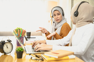 Wall Mural - Serious muslim woman having discussion on laptop, talking with assistant at co-workers, 
solemn at friends while sitting on table in working room