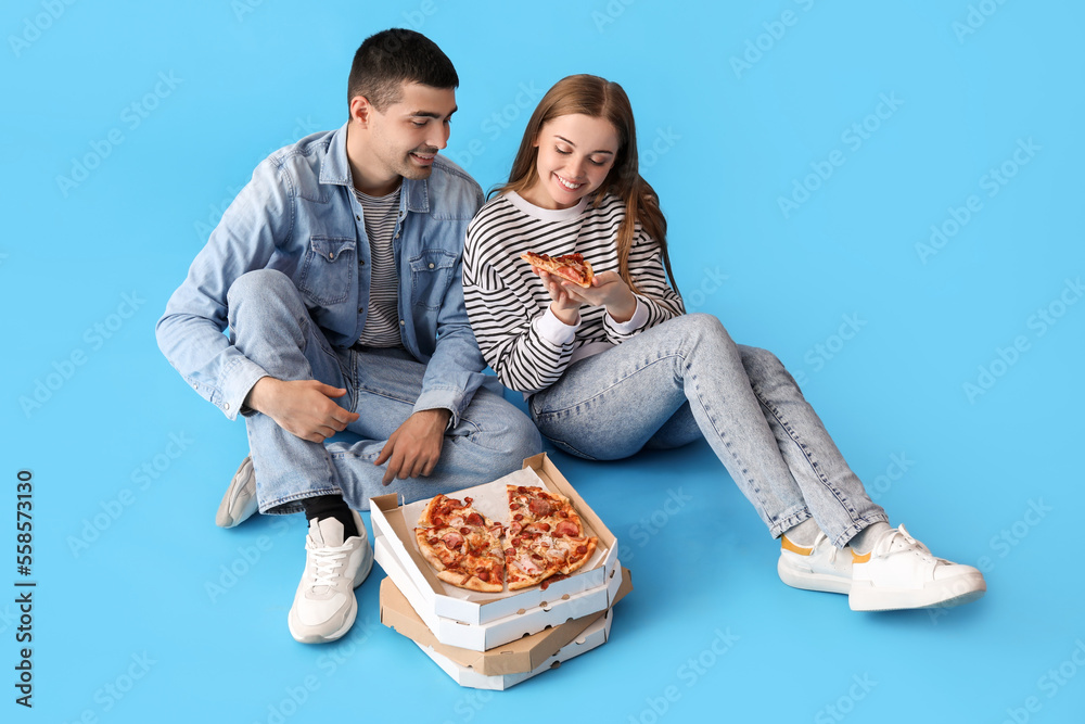 Happy young couple eating fresh pizza on blue background