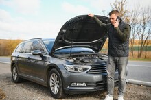 Man Repairing A Broken Car By The Road. Man Having Trouble With His Broken Car On The Highway Roadside. Man Looking Under The Car Hood. Car Breaks Down On The Autobahn. Roadside Assistance Concept.