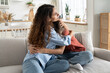 © DimaBerlin - Caring loving mother comforting hugging unhappy sad teenage daughter, sitting together on sofa at home, mom supporting depressed teen girl child, parent making peace with kid. Parenting of adolescents