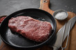 Entrecote Steak roh vom Rind mit Meersalz und roter Pfeffer auf Teller bei Vorbereitung in Küche mit Messer, Fleischgabel und Holz Brett auf Schiefer Stein Hintergrund Schwarz