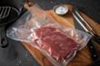 Entrecote Steak roh vakuumiert vom Rind mit Meersalz auf Teller bei Vorbereitung in Küche mit Messer, Fleischgabel, Gusseisern Pfanne, Plastik Vakuumbeutel und Pfannenwender auf Holzbrett und Schiefer