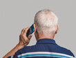 Back view of a senior man using a smartphone while standing on a gray background