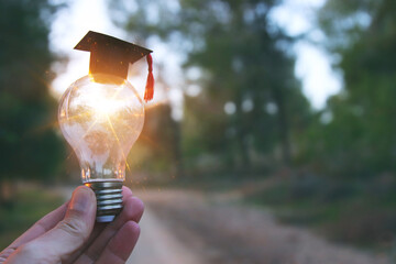 Poster - A hand holding a light bulb and graduation cap in front of the sun. Idea of education, technology, use of solar energy