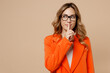 © ViDi Studio - Young employee business woman corporate lawyer wear classic formal orange suit glasses work in office say hush be quiet with finger on lips shhh gesture look aside isolated on plain beige background.