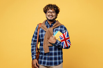 Wall Mural - Young fun happy teen Indian boy IT student he wear casual clothes shirt glasses bag hold in hands books British flag isolated on plain yellow color background High school university college concept.