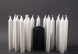 © Natalia - A group of white candles on a gray background. One black candle among the whites.