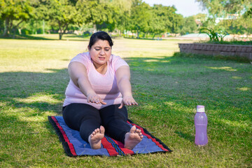 Wall Mural - Overweight indian woman doing stretching exercise outdoors in park while watching online training classes on her laptop. Asian Fat lady Fitness lifestyle. Full length shot.