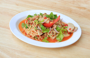 Wall Mural - Spicy Instant Noodle Salad with Sliced Vietnamese Pork Sausage in white plate on wood background - Thai food.