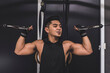 © Mdv Edwards - A fit asian man does standing overhead bicep cable curls. Wearing a black low cut tank top. Training arms at the gym.