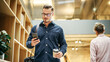 © Gorodenkoff - Portrait of White Man Walking in Office Hall With Smartphone and Coffee and Smiling. Male Software Developer Reading Feedback on His Work with Confidence. Low Angle, Close Up Shot
