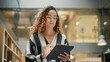 © Gorodenkoff - Female Data Analyst Smiling While Checking New Data for the Day. Portrait of hispanic Businesswoman Walking Towards her Business Office in a Spacious Corporate Building. Low Angle