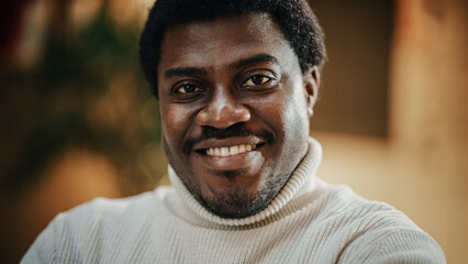 Wall Mural - Close-up Portrait of Handsome Black Man with Trimmed Beard, Wearing Stylish White Turtleneck, Smiling and Looking at the Camera. Confident Male Startup CEO Celebrating his Achievement