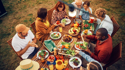 Wall Mural - Top Down Elevated View at a Family and Friends Celebrating Outside at Home. Diverse Group of Children, Adults and Seniors Sitting at a Table, Having Fun Conversations. Eating Barbecue and Vegetables.