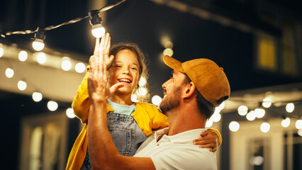 Wall Mural - Proud Handsome Father Helping His Little Beautiful Daughter to Change a Lightbulb in Fairy Lights Backyard Installation at Home. Father and Daughter High Five and Celebrate Successful Fix.