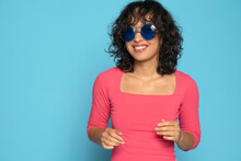 Young Exotic Smiling Brunette Woman In Pink Blouse Posing With A Sunglasses On A Blue Background