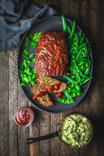 Meatloaf And Slices On Platter With Fresh Snap Peas, Mashed Potato In Pan, And Sauce In Jar
