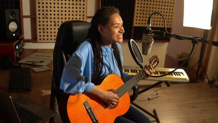 Wall Mural - Cheerful talented woman singer playing guitar and singing new cool song into a microphone in music recording studio