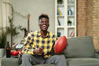 © JustLife - Young African man watching sport match on television and supporting his favorite team. Happy man enjoying victory, watching sports competition on tv.