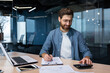 © Liubomir - Successful financier investor works with documents and accounts inside office, businessman with beard smiling satisfied with work results and achievements, man inside office with laptop working.
