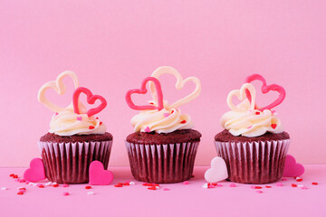 Poster - Valentines Day theme red velvet cupcakes with sweet hearts and creamy icing. Side view with a pink background.