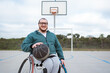 athlete in wheelchair smiling and looking at camera with ball in basketball court