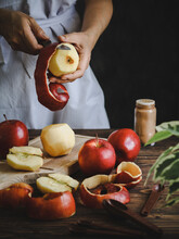 Woman Peeling Red Apples On A Cutting Board Over A Rustic Dark Wooden Table