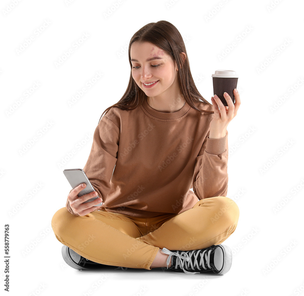 Pretty young woman with smartphone drinking coffee while sitting against white background