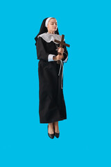 Young nun with cross jumping on blue background