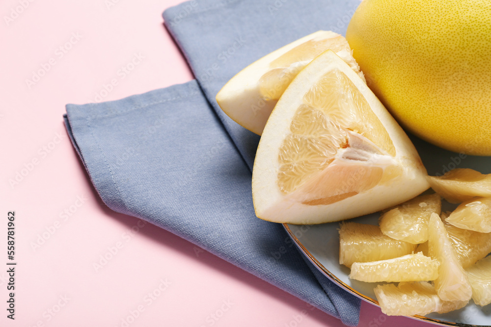 Plate with pomelo fruit and slices on pink background, closeup