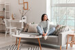 © Pixel-Shot - Young woman sitting on grey couch in living room