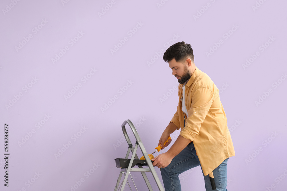 Young man with paint roller and ladder near lilac wall