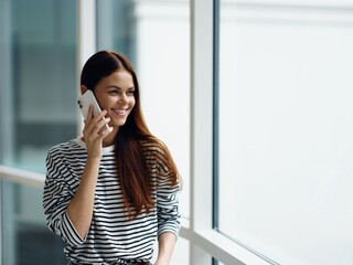 Woman smile talking on the phone video call online communication, woman at the window in the office in the city