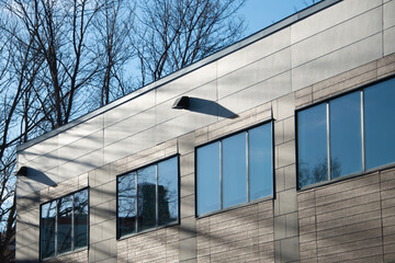 The exterior wall of a contemporary commercial style building with aluminum metal composite panels and glass windows. The futuristic building has engineered diagonal cladding steel frame panels.