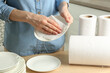 Woman wiping ceramic plate with paper towel indoors, closeup