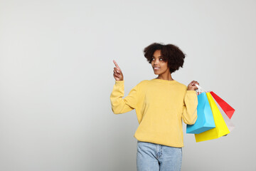 Wall Mural - African American woman with shopping bags on light grey background. Space for text