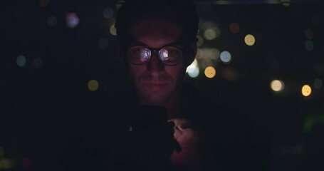 Portrait of young man using mobile phone, scrolling app pages social networks, mobile screen reflected on his face. Male in glasses scrolling internet on mobile phone background of night city.