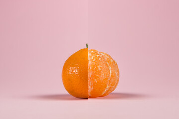 Two halves of a tangerine on a pink background. Half a peeled and unpeeled tangerine