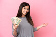 Young Brazilian woman taking a lot of money isolated on pink background extending hands to the side for inviting to come