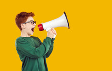 Happy Child Standing On Yellow Background Screaming Through Megaphone. Excited Smart Clever Redhead School Boy In Glasses And Green Sweatshirt Advertises New Science Centre For Kids. Side Profile View