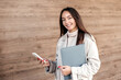 © Evgenia - A young woman holds a mobile phone and a folder in her hands wearing in a trench coat against the backdrop of an office building