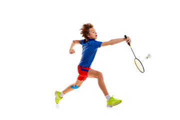 Wall Mural - Portrait of teen boy in uniform playing badminton, hitting shuttlecock with racket in a run isolated over white background