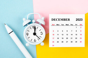 The December 2023 Monthly calendar with alarm clock and pen on beautiful background.