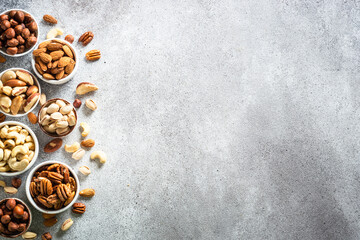 Wall Mural - Nuts in bowls at light background. Cashew, hazelnuts, pecan, almonds, brazilian nuts and pistachios. Top view with copy space.