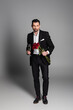 © LIGHTFIELD STUDIOS - Full length of man in formal wear holding red doses and champagne on grey background.