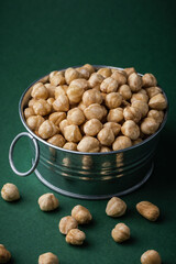 Wall Mural - A pile of peeled hazelnuts in a metal bowl on the green background Healthy nutrition concept. Traditional rustic agricultural background. Copy space for a free text