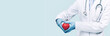 Female doctor in white uniform forms a heart shape with her hands. Minimal background. Banner copy space. Heart, cardiology and medical care support and assistance female health gynecology