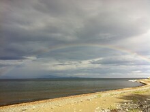 Rainbow Arching Over Gold Sand And Sea With Clearing Storm.