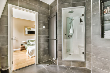 a modern bathroom with grey tile walls and white trim on the shower door, toiletries and mirror in the corner